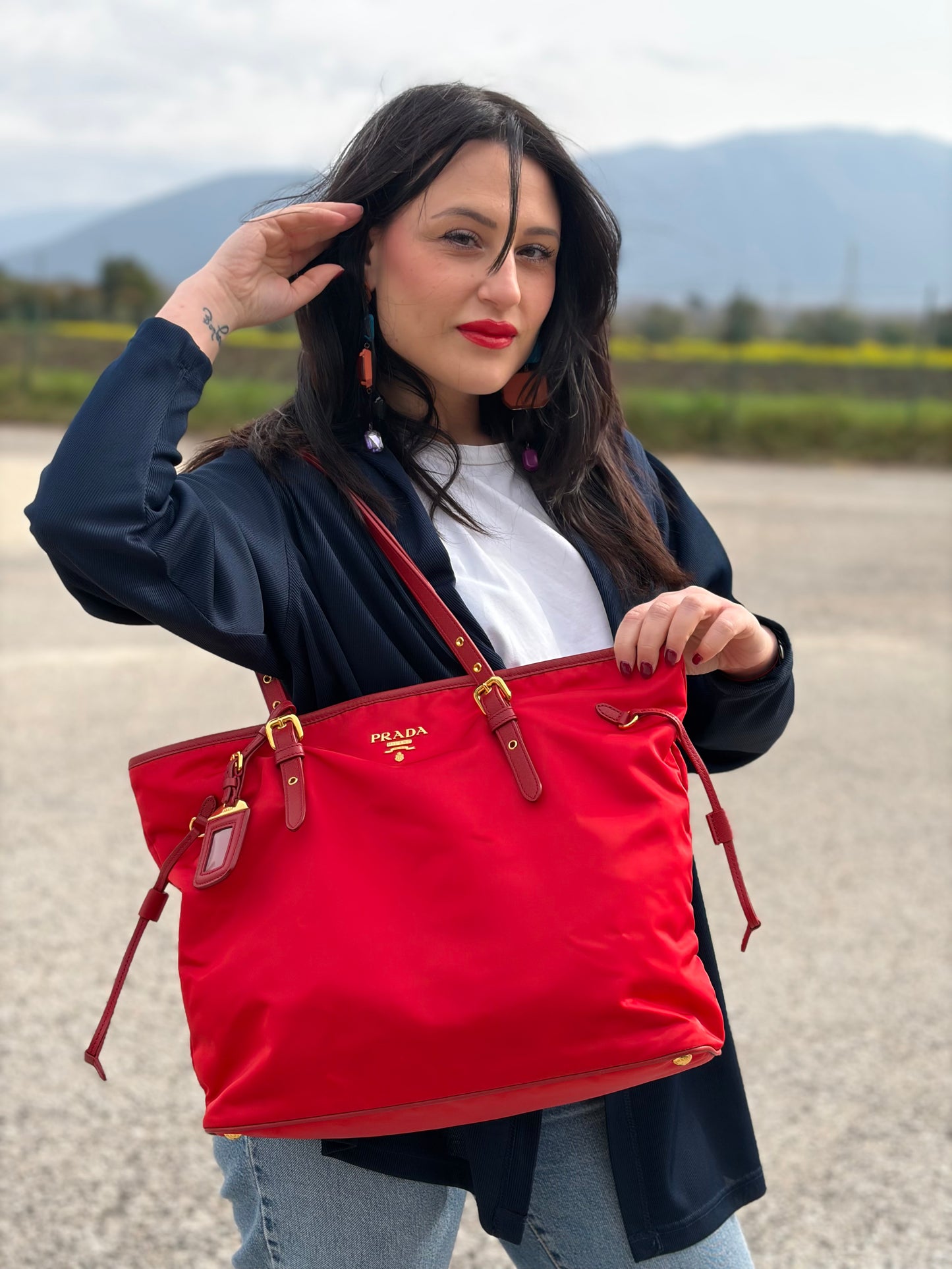 Ragazza che indossa una borsa Prada in nylon rosso e finiture in pelle saffiano tono su tono, usata, originale, second hand, in ottime condizioni.