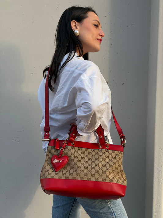 Ragazza che indossa una borsa Gucci in tessuto beige trama GG, con finiture in pelle rosse e romantico charm a forma di cuore, usata, originale, second hand, in ottime condizioni.