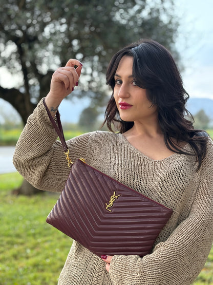 Ragazza che indossa una pochette Saint Laurent in pelle bordeaux trapuntata, con parti metalliche dorate, usata, originale, second hand, in ottime condizioni.