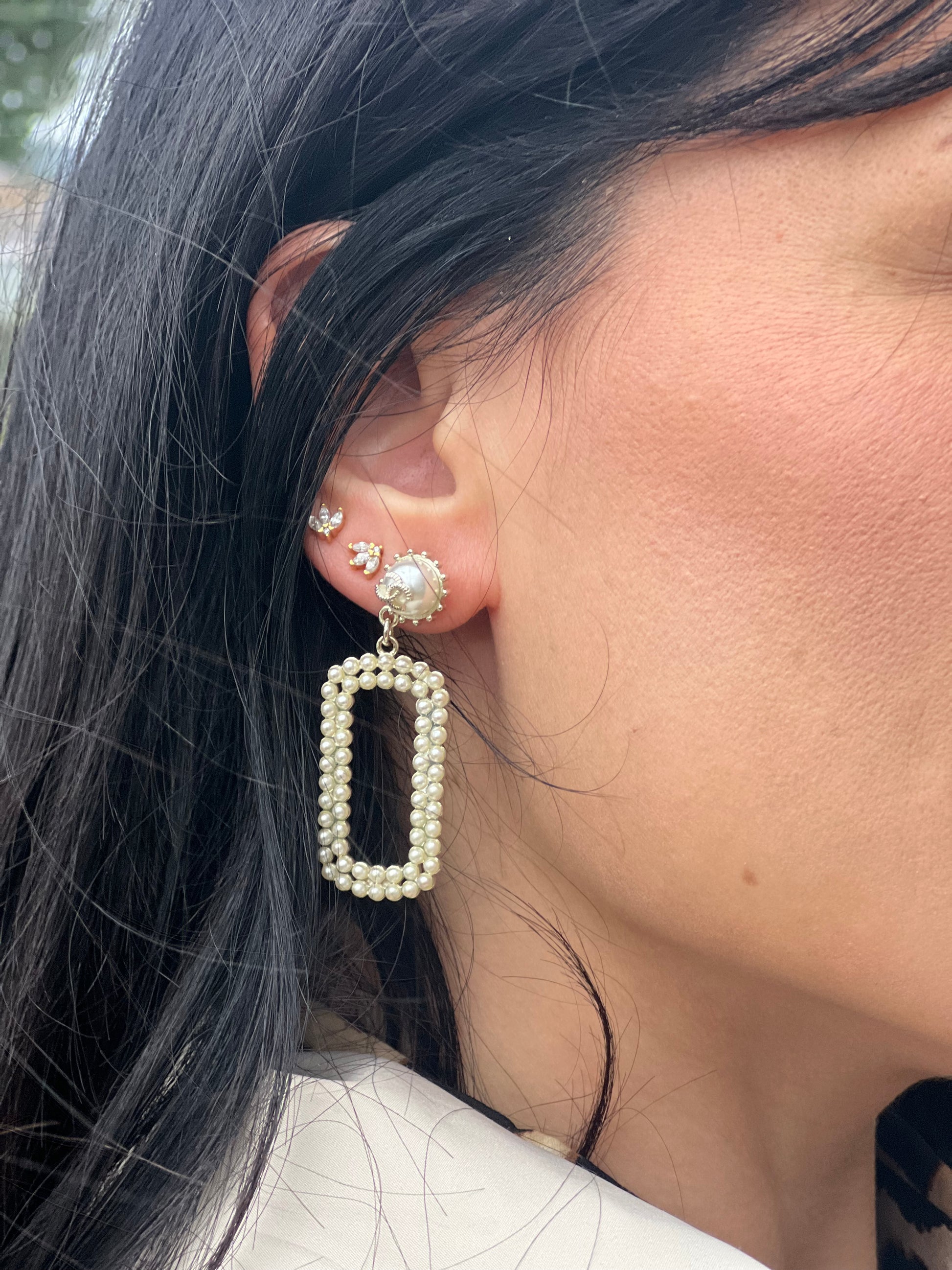 Ragazza che indossa degli orecchini Chanel dal design rettangolare pendente composto da piccole perle disposte in doppia fila. La parte superiore è decorata da una perla più grande con il logo CC in metallo. Full set.