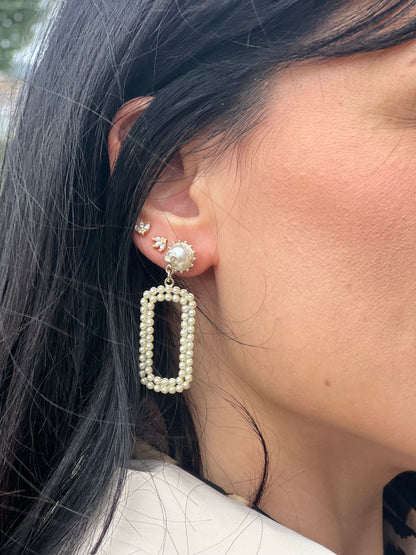 Ragazza che indossa degli orecchini Chanel dal design rettangolare pendente composto da piccole perle disposte in doppia fila. La parte superiore è decorata da una perla più grande con il logo CC in metallo. Full set.