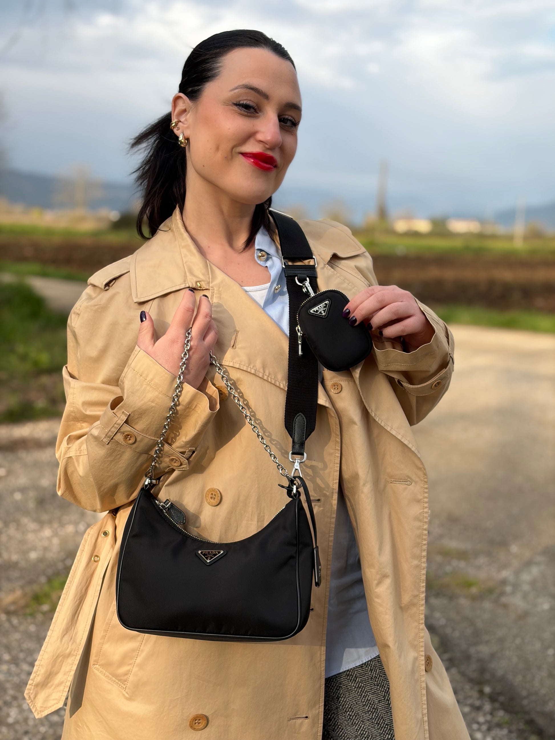 Ragazza che indossa una borsa Prada Re-Edition 2005 in nylon nero con dettagli in pelle e hardware argento, arricchita da catena frontale, mini pouch removibile e portachiavi logato. Modello compatto e versatile, utilizzabile a spalla, a mano o crossbody, usata, originale, second hand, in condizioni eccellenti.