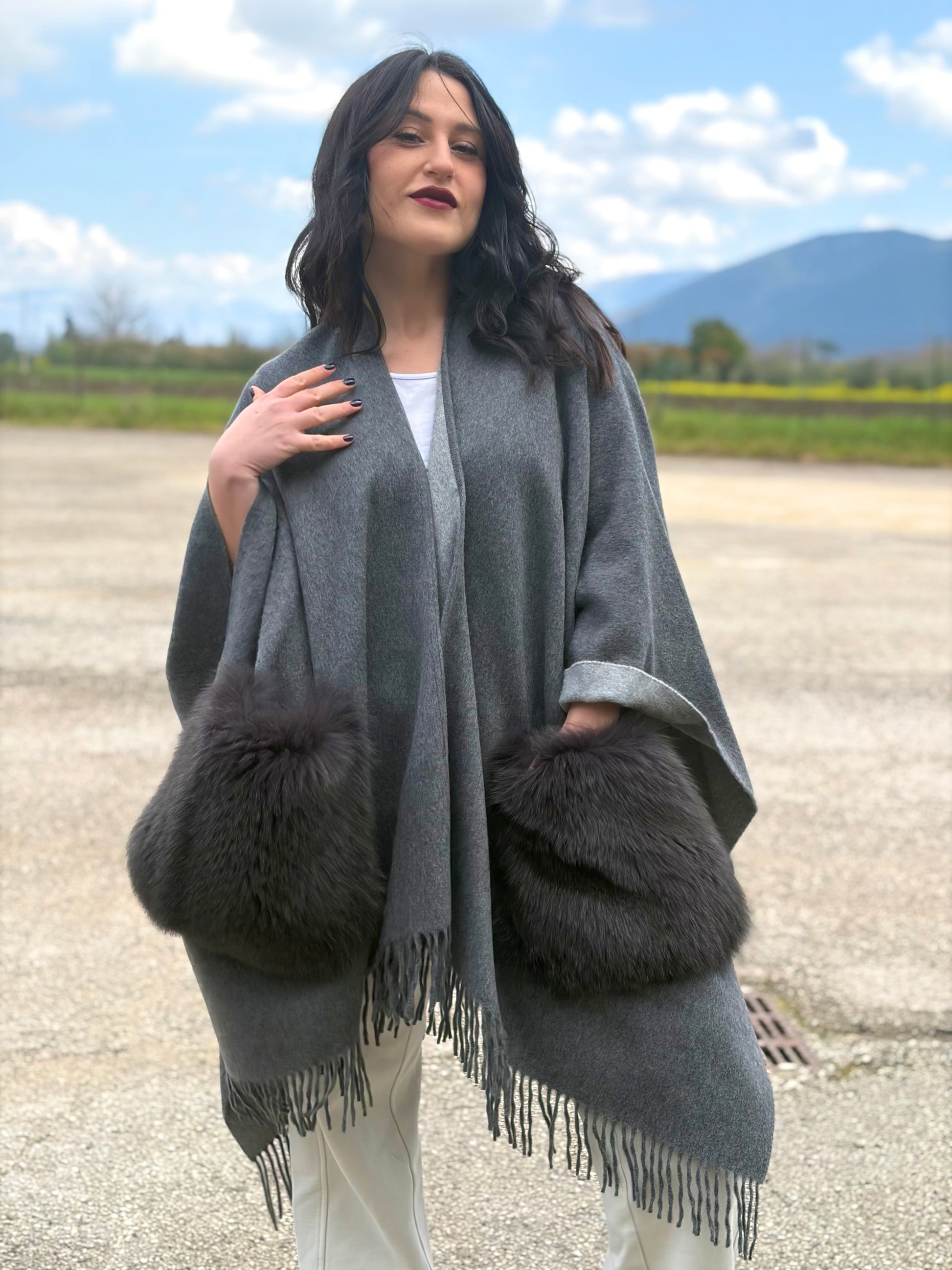 Ragazza che indossa un poncho Herno in morbida lana grigia con tasconi in pelliccia e bordi sfrangiati, usato, originale, second hand, in ottime condizioni.