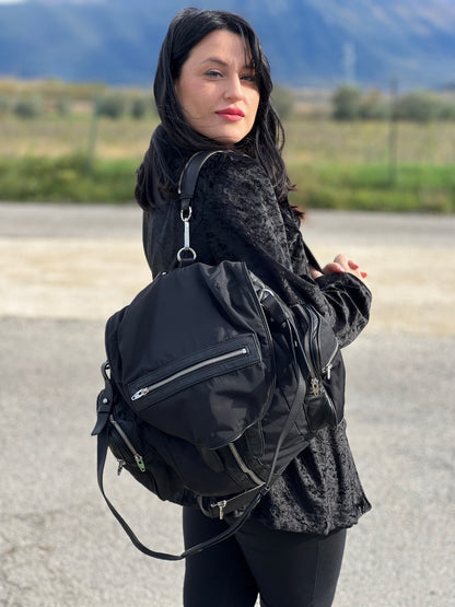 Ragazza che indossa uno zaino Alexander Wang in nylon nero e finiture in pelle tono su tono. Parti metalliche argentate; munito di doppie bretelle e una tracolla. Indossabile come zaino o a tracolla.