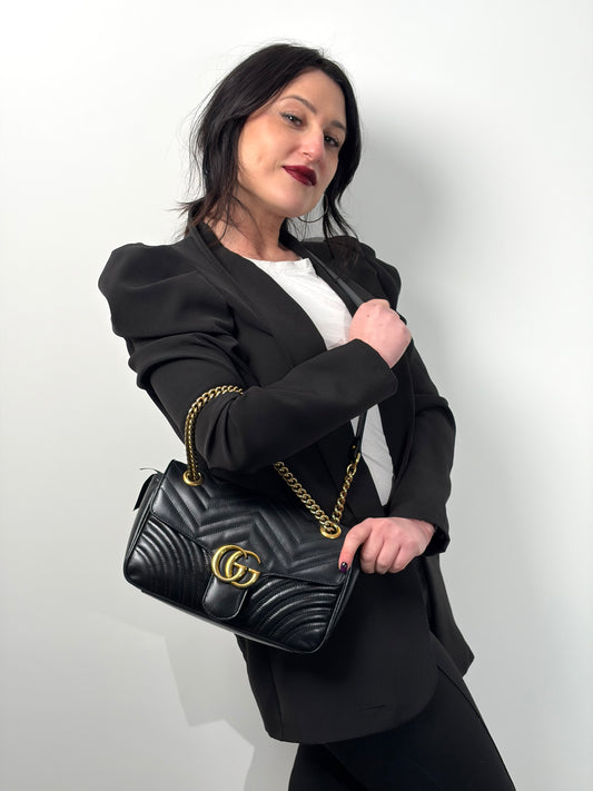 Ragazza che indossa una borsa Gucci Marmont nera in pelle con motivo chevron nella misura media, usata, originale, second hand, in ottime condizioni.