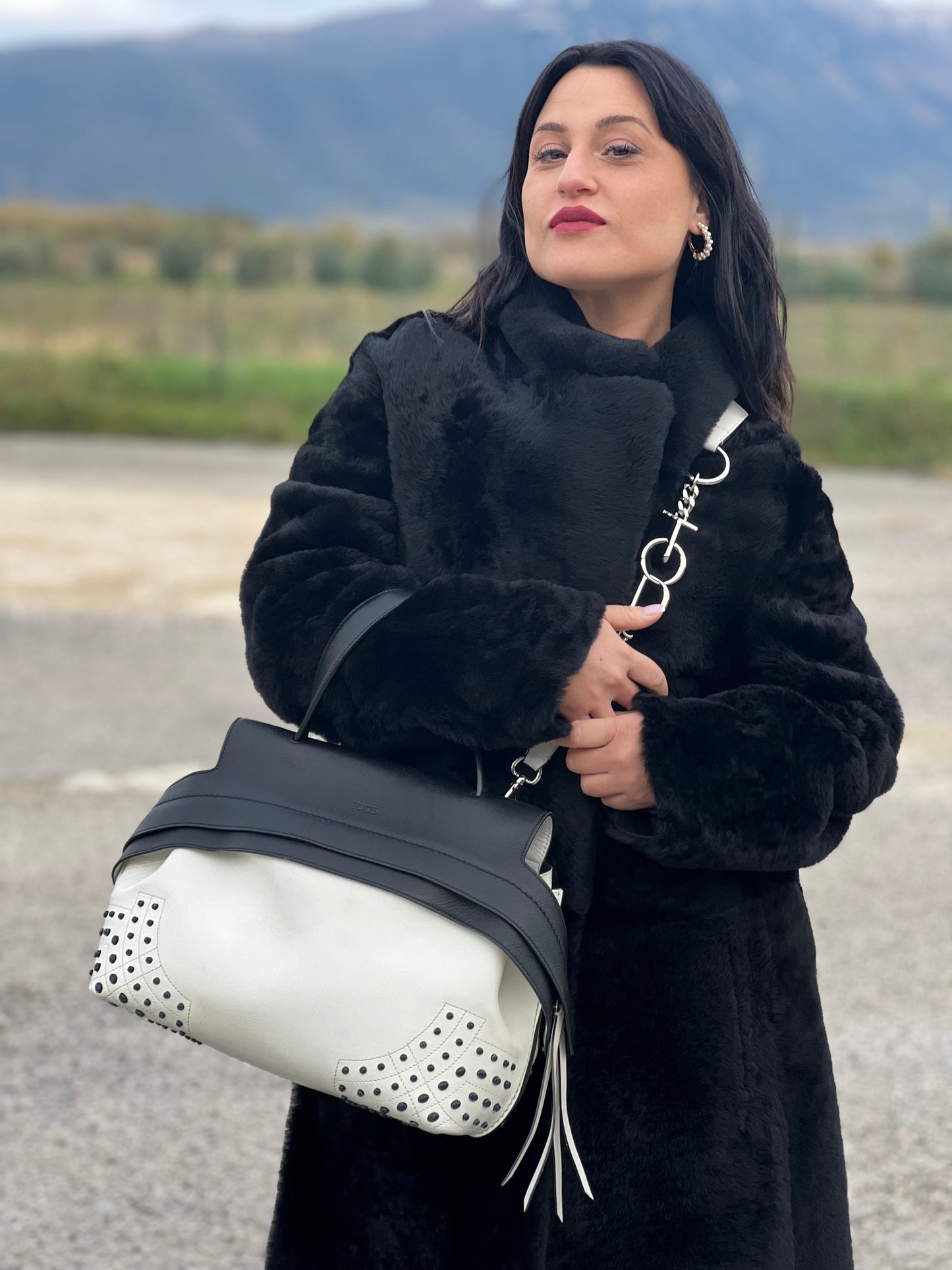 Ragazza che indossa una borsa Wave Tod's in pelle bianca e nera impreziosita da iconici gommini Tod's sugli angoli della base. Munita di un manico singolo stondato, una tracolla con lettere in catena e pelle, regolabile ed amovibile. Parti metalliche argentate. Dotata di dustbag.