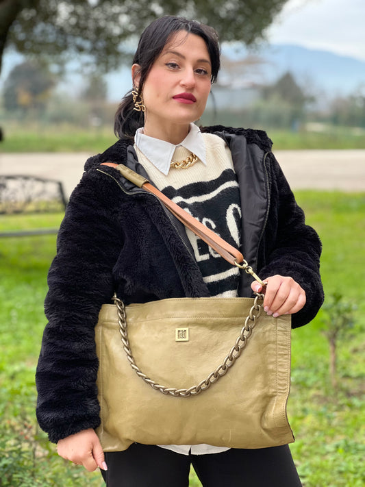 Ragazza che indossa una borsa A.S. 98 in pelle color oliva, dotata di tracolla regolabile in pelle e catena metallica dorata. Presenta chiusura con zip, tasche interne e fodera stampata. Munita di dustbag.