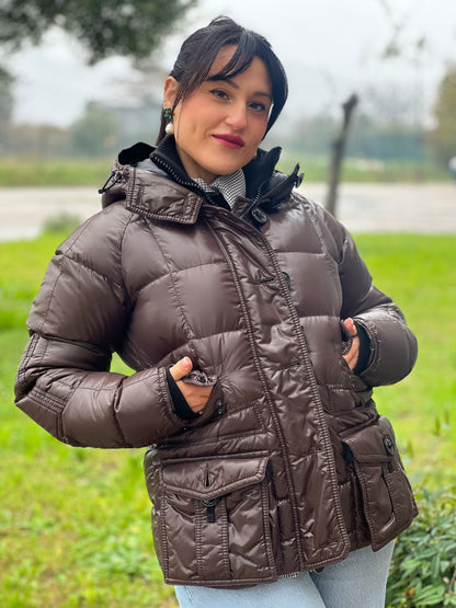 Ragazza che indossa un piumino Moncler in tessuto lucido color marrone, con parti metalliche effetto renio, in 100% poliammide, caratterizzato da imbottitura trapuntata, chiusura con zip e bottoni logati, cappuccio regolabile e polsini interni a coste per una maggiore protezione dal freddo.