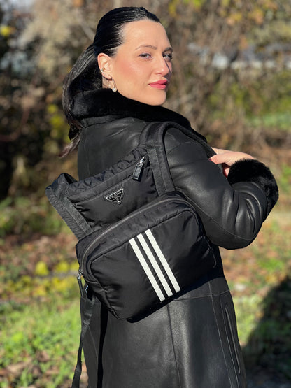 Ragazza che indossa uno zaino Prada x Adidas in Re-Nylon con chiusura a zip. Struttura con tasca frontale a zip e tasca superiore integrata negli spallacci. Spallacci regolabili con imbottitura e pannello posteriore in mesh. Dettagli con logo triangolo Prada sul lato superiore e branding Prada Re-Nylon e Adidas sul fianco.