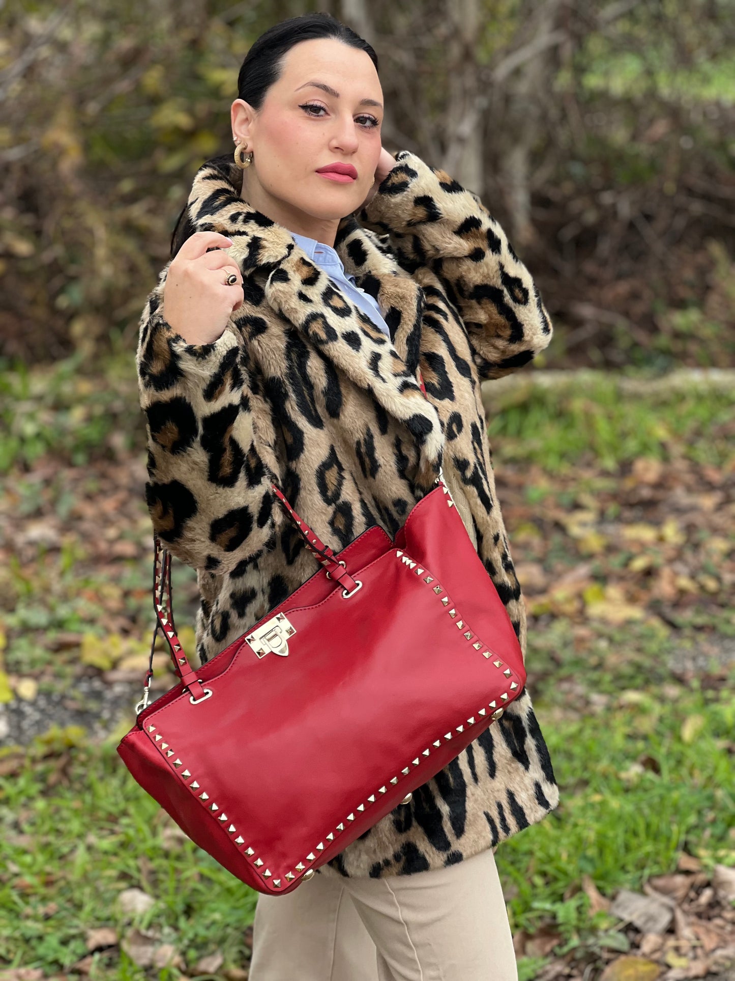 Ragazza che indossa di una borsa Valentino Garavani in pelle rossa con parti metalliche dorate; impreziosita da borchie piramidali e munita di doppi manici e tracolla amovibile. Completa di dustbag. 