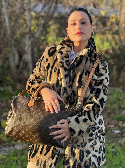 Ragazza che indossa una borsa Speedy 30 in canvas marrone monogram con finiture in vacchetta naturale e parti metalliche dorate; munita di doppi manici stondati e una tracolla amovibile e regolabile. Completa di corredo, lucchetto e chiavi.