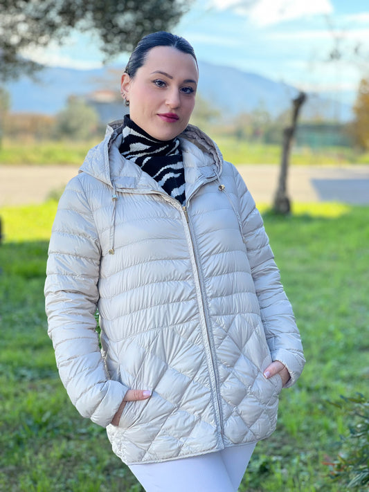 Ragazza che indossa un piumino Max Mara The Cube in 100% poliammide trapuntato, colore avorio perla. Modello con cappuccio, coulisse regolabile in vita e dettagli metallici dorati. Chiusura con zip.
