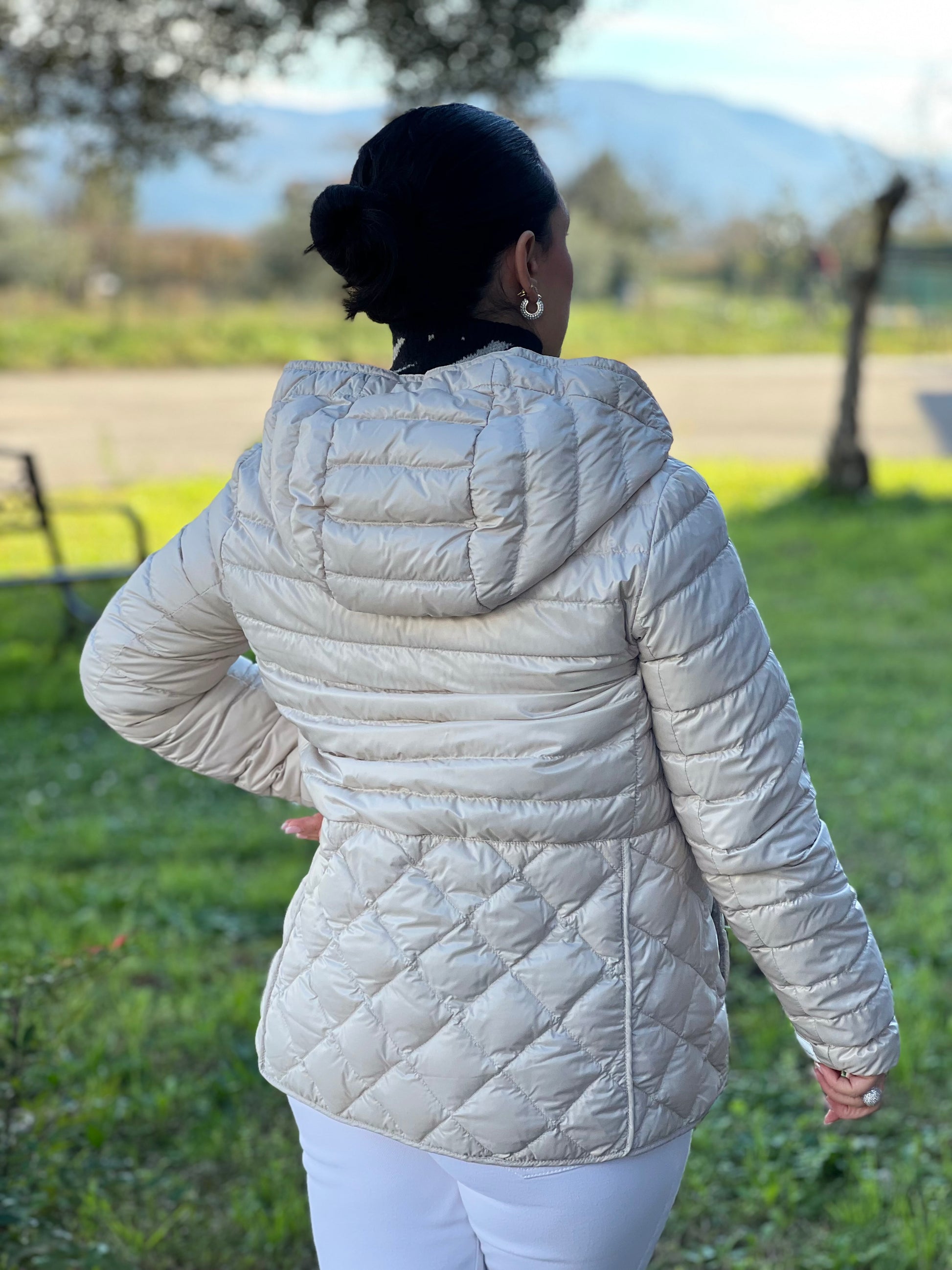 Ragazza che indossa un piumino Max Mara The Cube in 100% poliammide trapuntato, colore avorio perla. Modello con cappuccio, coulisse regolabile in vita e dettagli metallici dorati. Chiusura con zip.