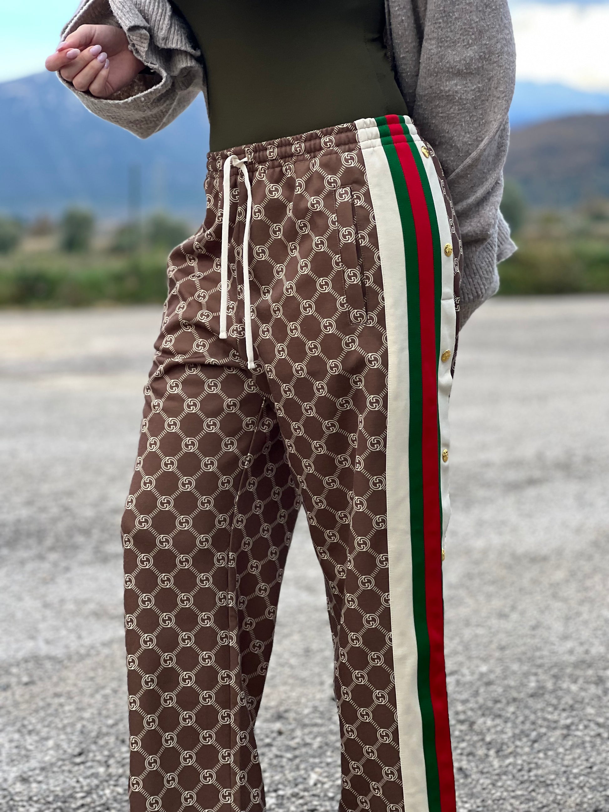 Ragazza che indossa un pantalone tuta Gucci elasticizzato modello Interlocking G in 55% poliestere e 45% cotone, marrone e avorio con motivo GG all-over e bande laterali con bottoni automatici che si aprono fino ai fianchi, con strisce Web verde/rosse.