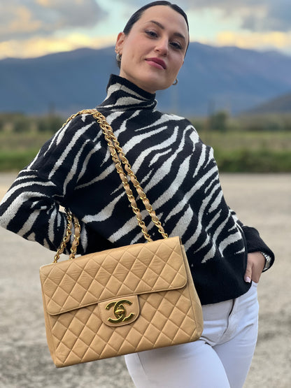Ragazza che indossa una borsa Chanel in pelle beige matelassè e parti metalliche dorate; munita di una tracolla scorrevole in catena e pelle. Indossabile a spalla e a tracolla. Completa di scatola, dustbag e card d'autenticità.