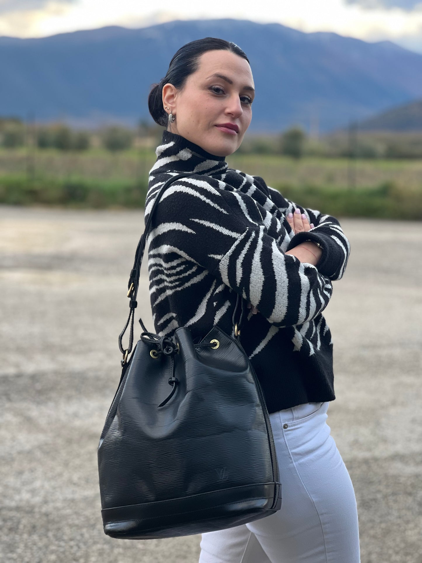 Ragazza che indossa un secchiello Noé Louis Vuitton in pelle Epi nera, con parti metalliche dorate e manico regolabile con fibbia. Indossabile a spalla. Completa di dustbag.