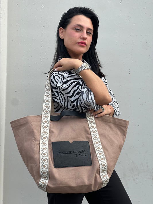 Ragazza che indossa una shopper Coccinelle in cotone beige con dettaglio manici a nastro intessuti in avorio; finiture in pelle nere, da indossare a spalla.