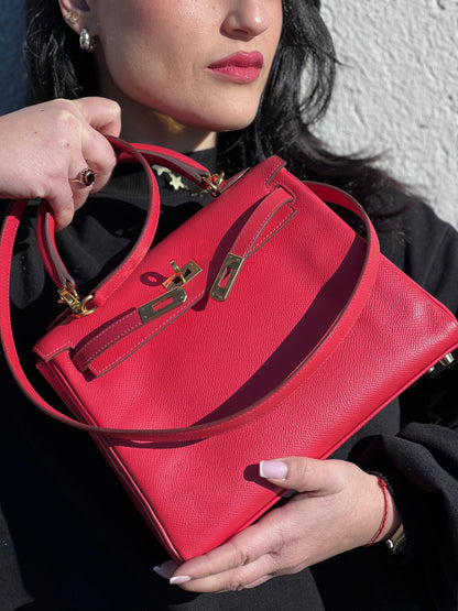 Ragazza che mostra una borsa Hermès caratterizzata da un corpo in pelle Epsom color Rouge Casaque, un manico superiore e una tracolla piatta rimovibile e non regolabile; da portare a mano o a tracolla. Completa di full set.