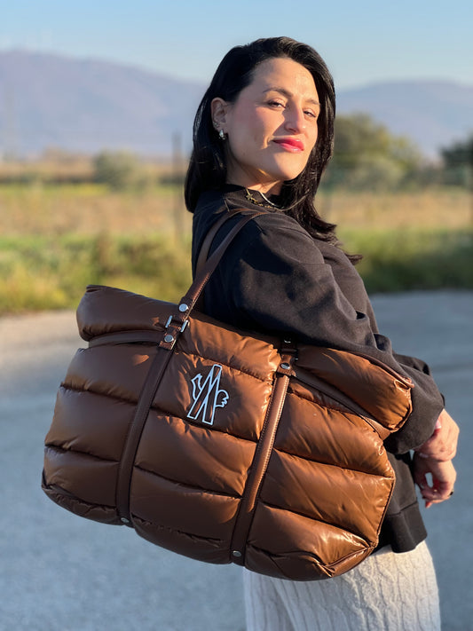 Ragazza che indossa una borsa Moncler in poliuretano color caramello effetto imbottito e finiture in pelle tono su tono, con metalleria dorata. Munita di cartellino. Da indossare a spalla.
