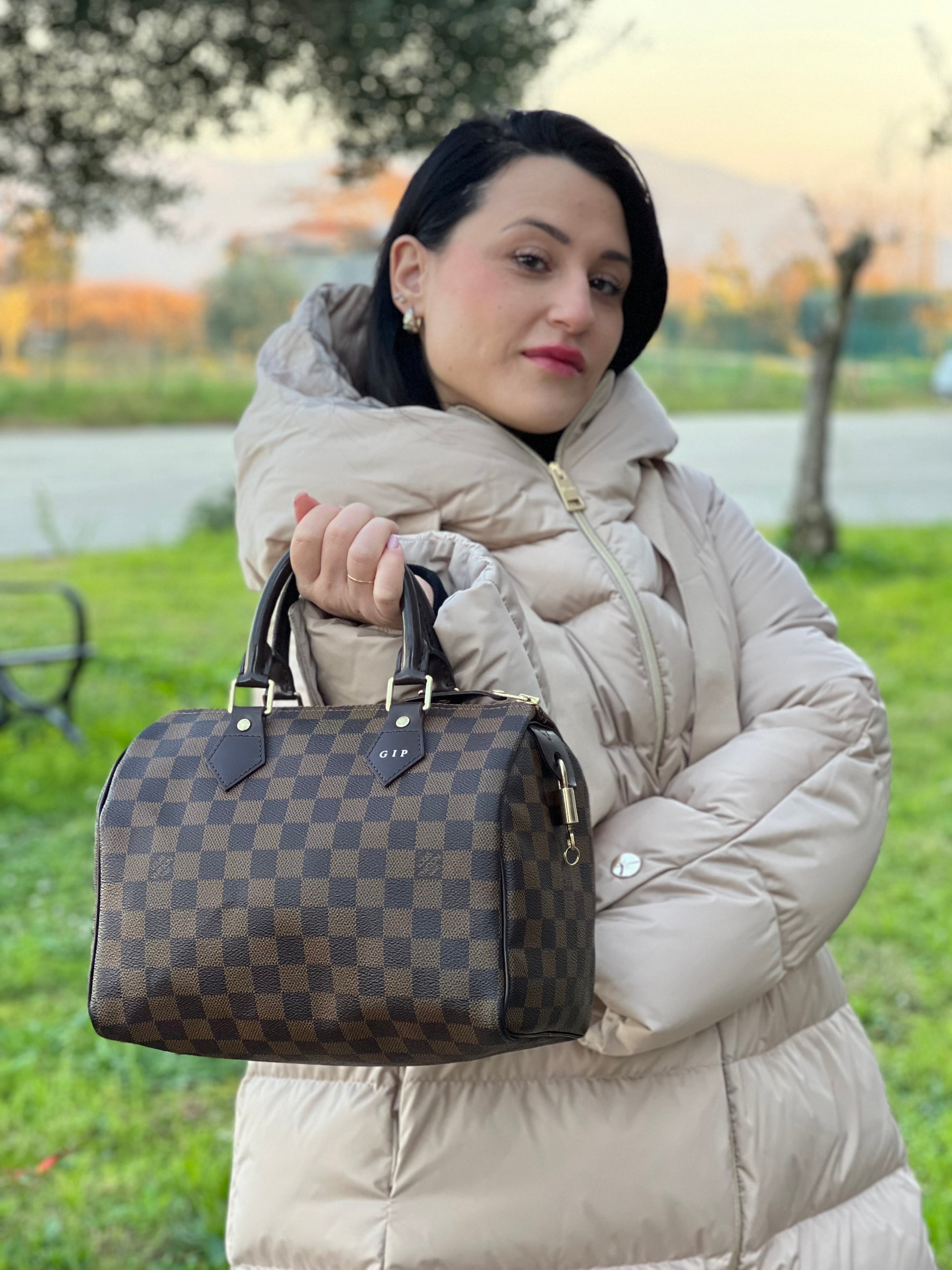 Ragazza che indossa una borsa Louis Vuitton in canvas Damier Ébène con parti metalliche dorate; munita di doppi manici stondati, da portare a mano. Completo di scatola logata, lucchetto e chiavi.