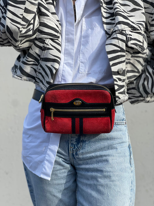 Ragazza che indossa un marsupio Gucci Ophidia in pelle scamosciata rossa con finiture in pelle verniciata nera, striscia Web centrale in tessuto blu e rosso, cintura regolabile e amovibile, parti metalliche dorate. Completo di dustbag.