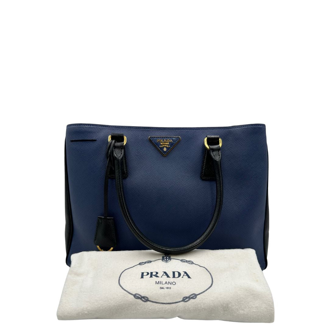 dustbag Borsa Prada in pelle saffiano blu e nera con parti metalliche dorate; munita di doppi manici stondati e impreziosita da un portachiavi. Completa di dustbag, di lusso, originale, ottime condizoni, usata. 