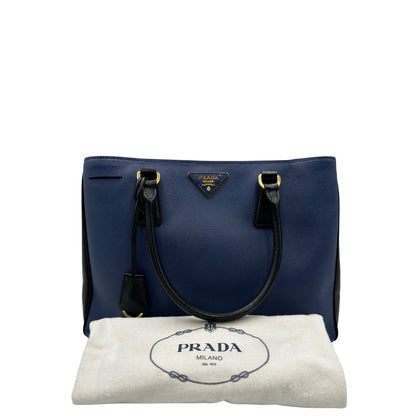 dustbag Borsa Prada in pelle saffiano blu e nera con parti metalliche dorate; munita di doppi manici stondati e impreziosita da un portachiavi. Completa di dustbag, di lusso, originale, ottime condizoni, usata. 