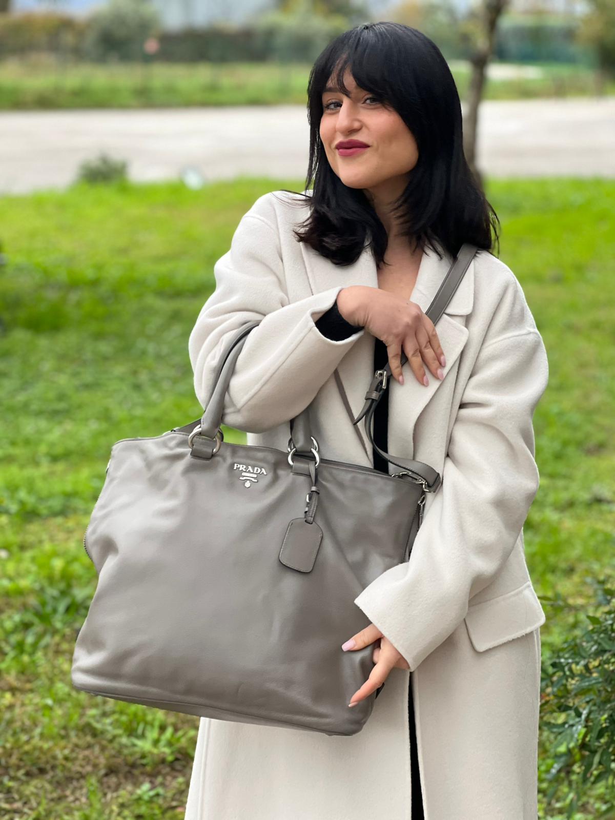 indossata Borsa Prada in pelle grigia con parti metalliche argentate; impreziosita da zip laterali e accessorio porta address, munita di doppi manici stondati e una tracolla amovibile e regolabile. Completa di dustbag, di lusso, originale, ottime condizioni. 