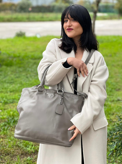 indossata Borsa Prada in pelle grigia con parti metalliche argentate; impreziosita da zip laterali e accessorio porta address, munita di doppi manici stondati e una tracolla amovibile e regolabile. Completa di dustbag, di lusso, originale, ottime condizioni. 