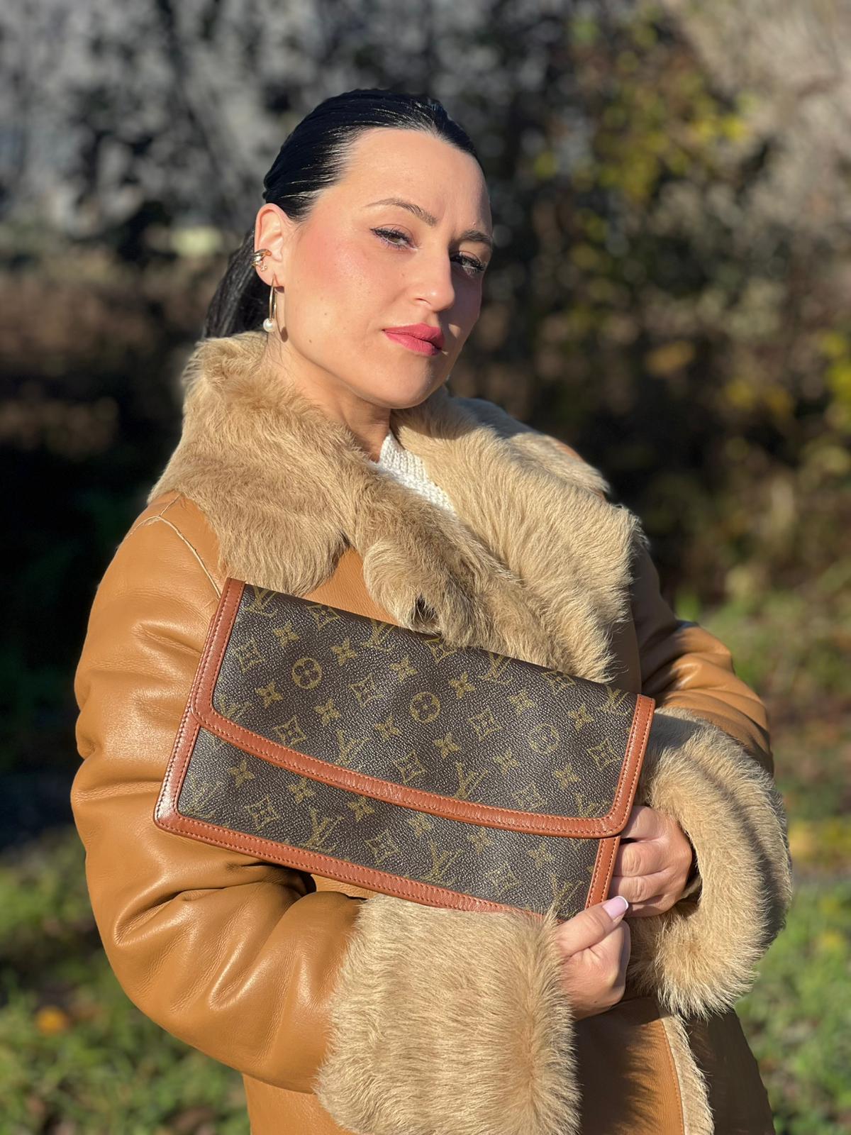 indossata della Pochette Louis Vuitton in canvas marrone monogram con finiture in pelle marroni e parti metalliche dorate; da portare a mano, di lusso, originale, ottime condizioni, usata.