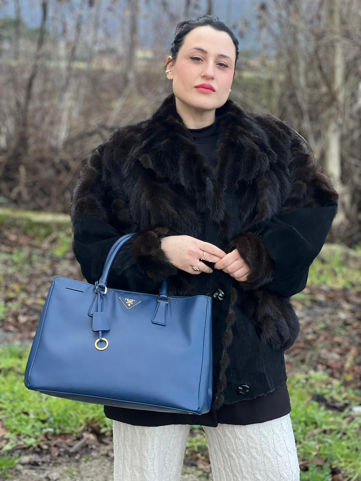 indossata  della Borsa Prada in pelle saffiano blu con parti metalliche dorate; munita di doppi manici stondati e impreziosita da una clochette portachiavi, di lusso, originale, ottime condizioni, usata.