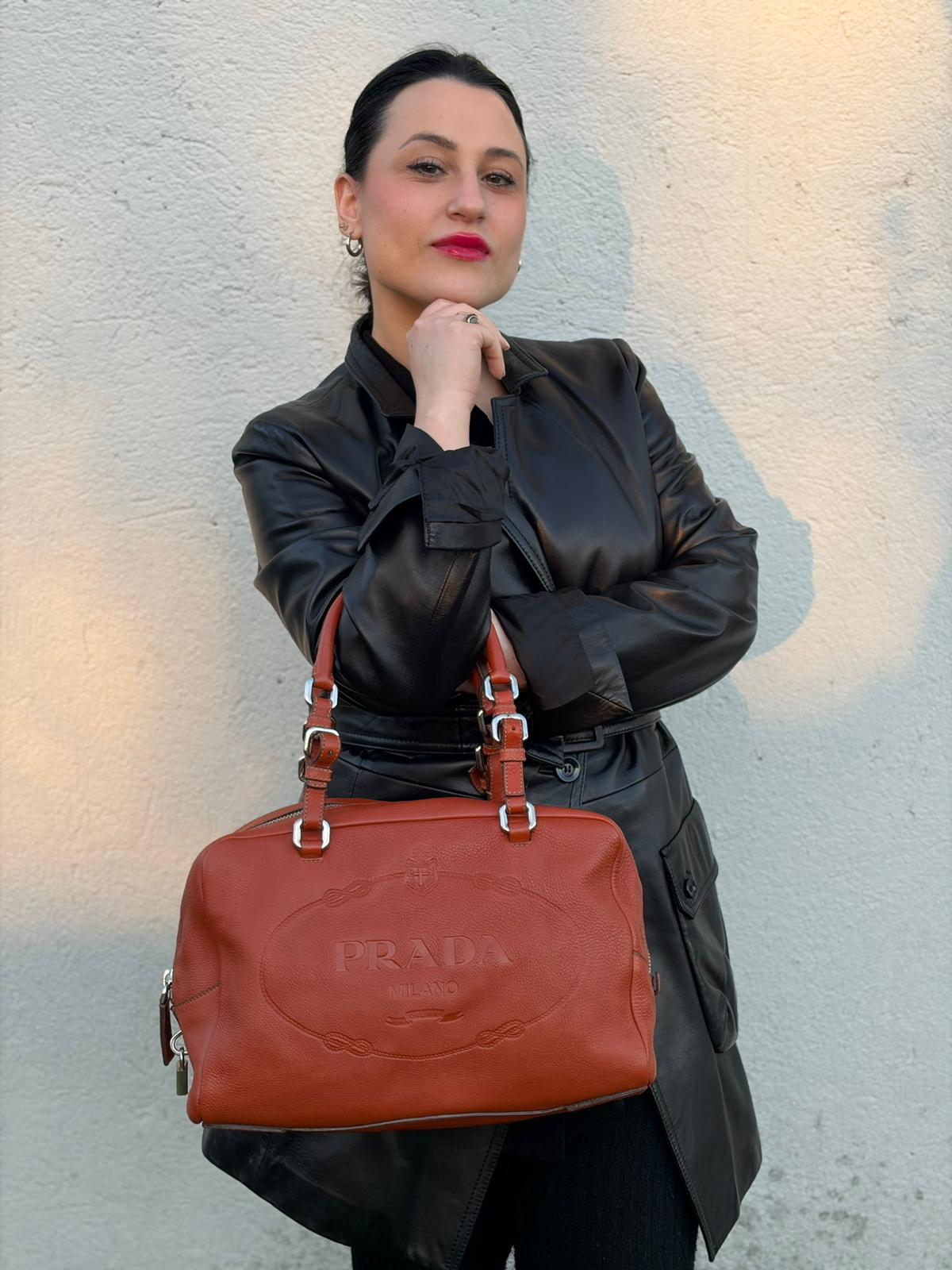 indossata della  Borsa Prada in pelle martellata color cognac con parti metalliche argentate; munita di doppi manici, indossabile a spalla. Completa di lucchetto e chiavi, di lusso, originale, ottime condizioni, usata. 