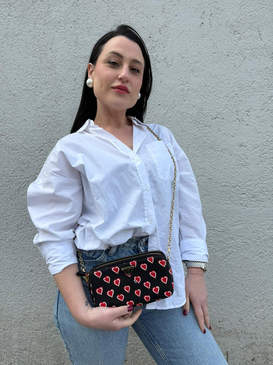 Indossata, Prada WOC in pelle saffiano nera decorata con una vivace stampa a cuori rossi. indossabile a tracolla oppure a mano. Originale, usata, di lusso, in ottime condizioni.