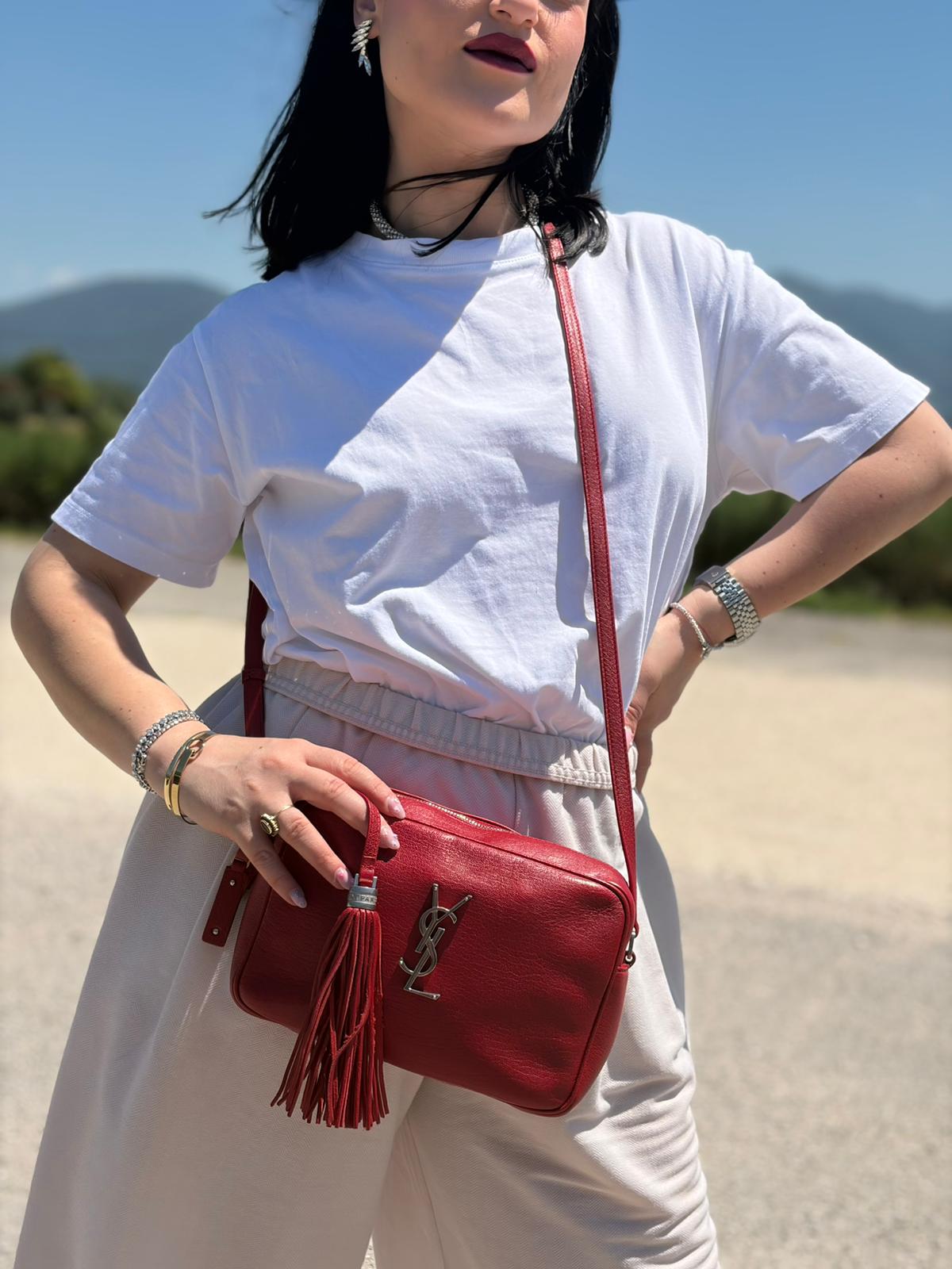 Indossata, Borsa Saint Laurent in pelle rossa con hardware argentato decorativo, iconiche iniziali YSL al centro e nappa decorativa. Indossabile a tracolla. Originale, usata, di lusso, in ottime condizioni.