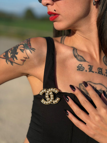Indossata, Elegante Spilla Chanel con iconico logo CC intrecciato in metallo dorato, impreziosito di perle decorative. Originale, usata, di lusso, in ottime condizioni.