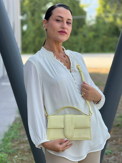 Ragazza chi indossa  Borsa Jacquemus in pelle glacé color giallo burro con parti metalliche dorate, munita di una tracolla regolabile e amovibile e un manico singolo
