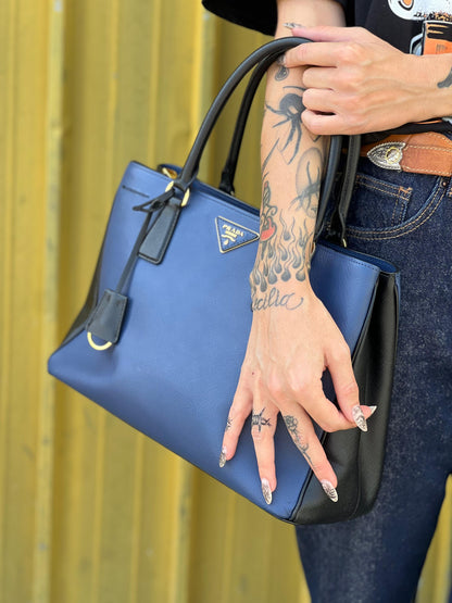 indossata interno Borsa Prada in pelle saffiano blu e nera con parti metalliche dorate; munita di doppi manici stondati e impreziosita da un portachiavi. Completa di dustbag, di lusso, originale, ottime condizoni, usata.  