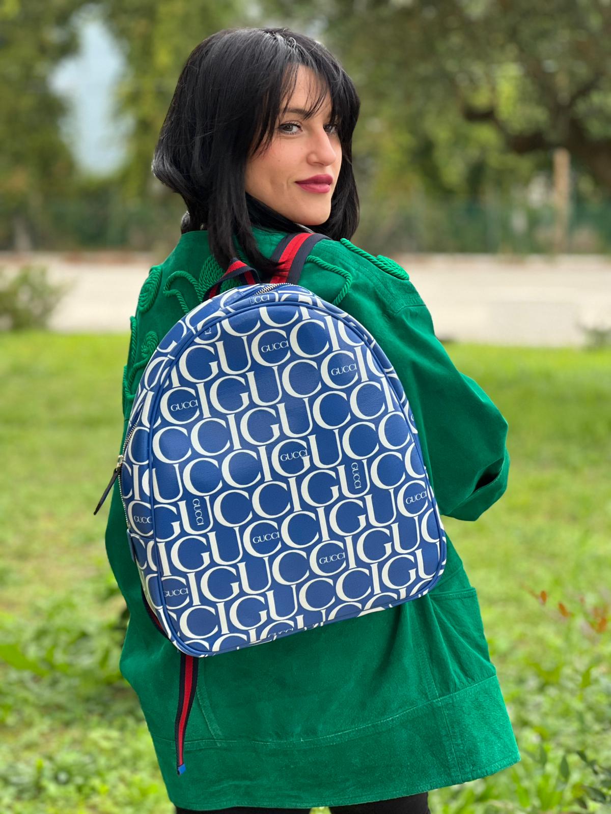 Ragazza chi indossa  Zaino Gucci in canvas blu e bianco monogram con parti metalliche dorate; munito di un manico e doppie bretelle con iconica trama Web blu e rossa. Completo di dustbag. Originale, usata, di lusso, in condizioni eccellenti.