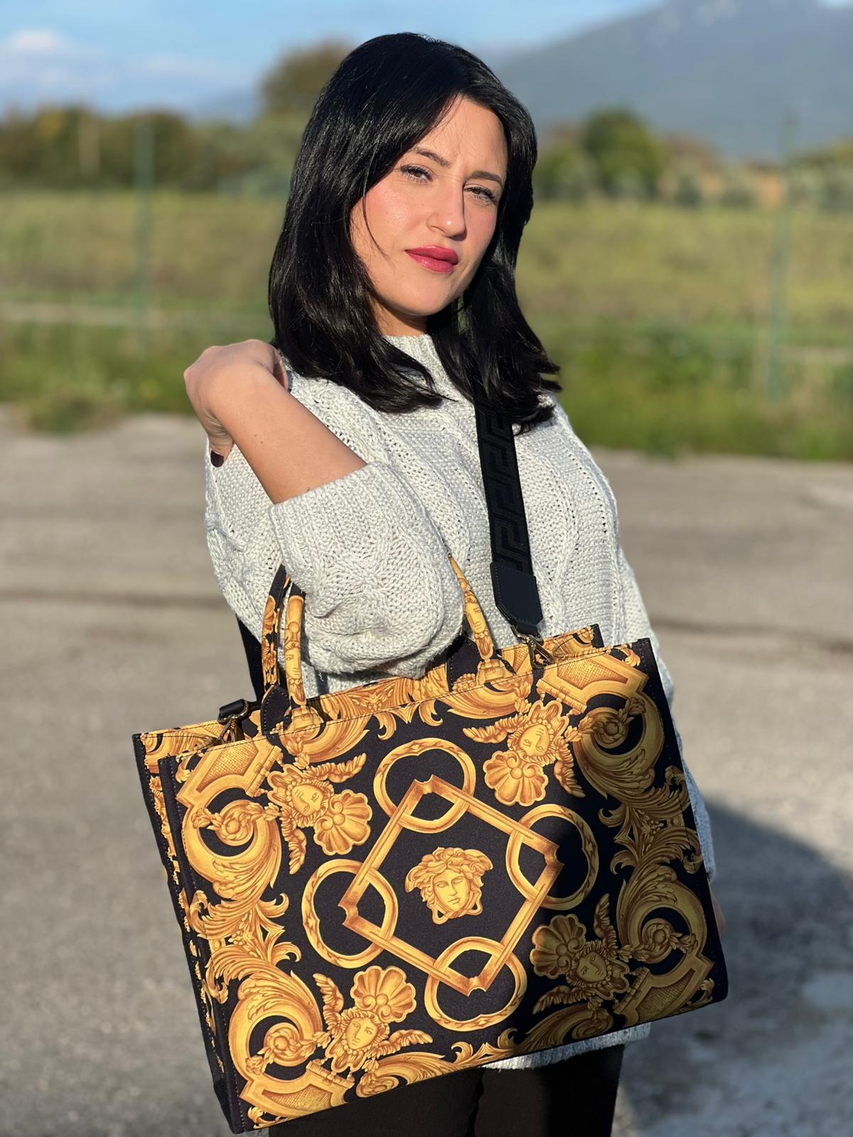 Ragazza che indossa una borsa Versace in tela com motivo jacquard barocco in nero e giallo tipico della Maison. Presenta doppi manici stondati e una tracolla amovibile in tessuto motivo greca, con dettagli in pelle neri. Completa di dustbag.