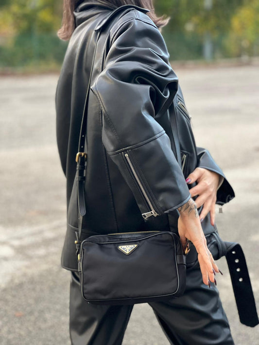 Ragazza che indossa una Borsa Prada in nylon nero con dettagli metallici dorati. Munita di una tracolla amovibile, e regolabile con spallaccio. Originale, usata, di lusso, in ottime condizioni