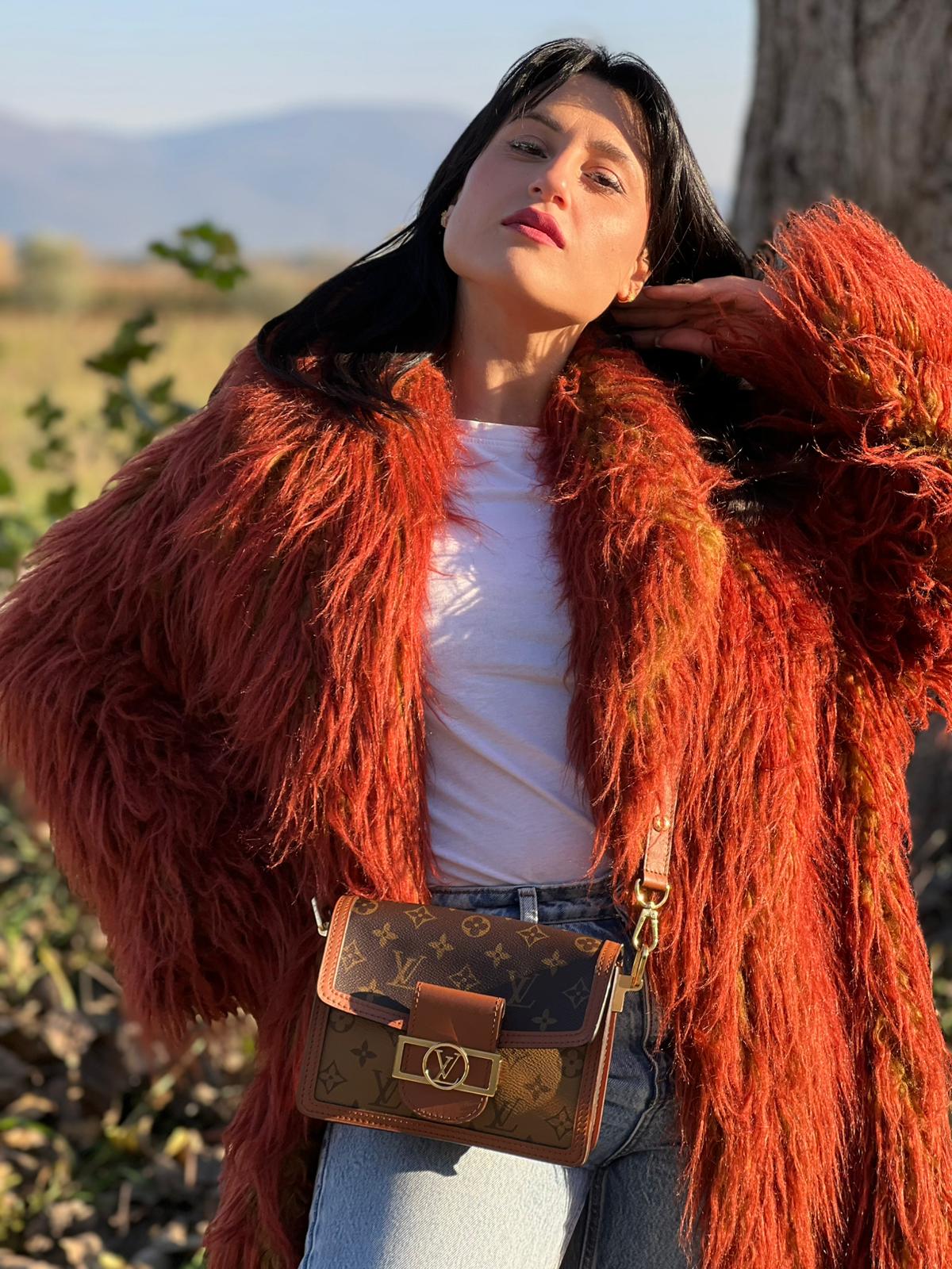 Ragazza che indossa una Borsa Dauphine Mini Louis Vuitton in tela monogram, e monogram reverse bicolore con finiture in pelle cognac e parti metalliche dorate, munita di una tracolla in pelle allungabile e un manico in catena, amovibili. Originale, usata, di lusso, in ottime condizioni