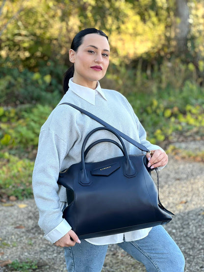 Ragazza che indossa una Borsa Givenchy Antigona in pelle blu notte munita di doppi manici stondati, Parti metalliche dorate e una tracolla amovibile. Completa di dustbag. Originale, usata, di lusso, in ottime condizioni.