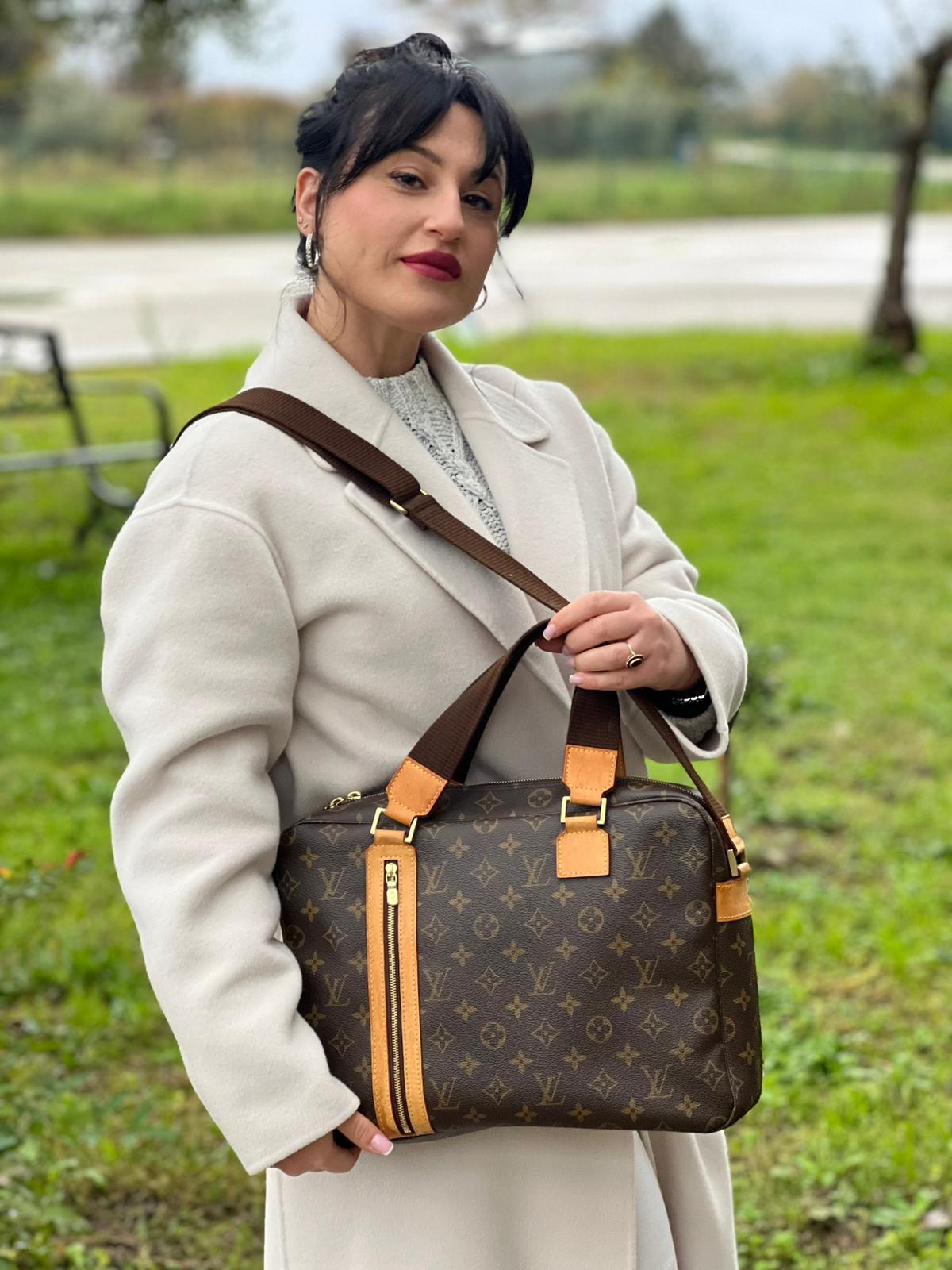 Ragazza che indossa una Borsa Louis Vuitton in canvas marrone monogram con finiture in vacchetta naturale e parti metalliche dorate; munita di due manici e una tracolla in tessuto regolabile. Completa di dustbag. Originale, usata, di lusso, in ottime condizioni.