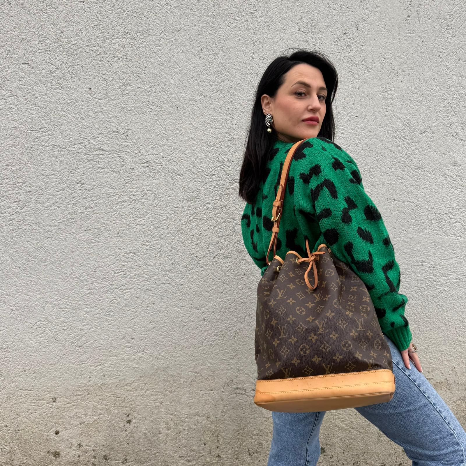 Ragazza che indossa un Secchiello Noé Louis Vuitton in canvas marrone monogram con finiture in vacchetta naturale, tracolla regolabile con fibbia e parti metalliche dorate. Completo di dustbag. Originale, usato, di lusso, in ottime condizioni