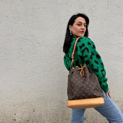 Ragazza che indossa un Secchiello Noé Louis Vuitton in canvas marrone monogram con finiture in vacchetta naturale, tracolla regolabile con fibbia e parti metalliche dorate. Completo di dustbag. Originale, usato, di lusso, in ottime condizioni