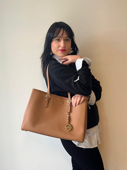 Ragazza che indossa una  Borsa Michael Kors in pelle saffiano color cammello con parti metalliche dorate, munita di doppi manici. Indossabile a spalla. Originale, usato, di lusso, in condizioni eccellenti.