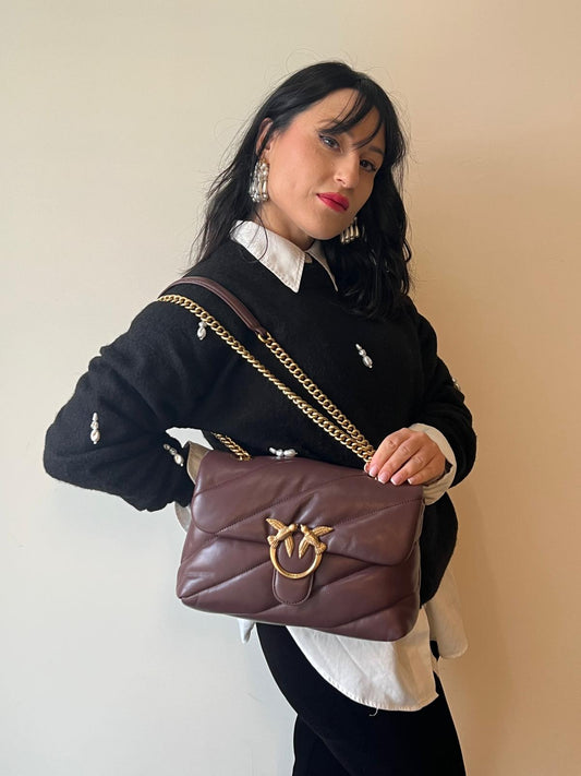 Ragazza che indossa un Borsa Pinko in pelle nera trapuntata color borgogna con parti metalliche dorate; munita di una tracolla in catena scorrevole e spallaccio in pelle. Completa di dustbag e cartellino. Originale, usata, di lusso, ottime condizioni.