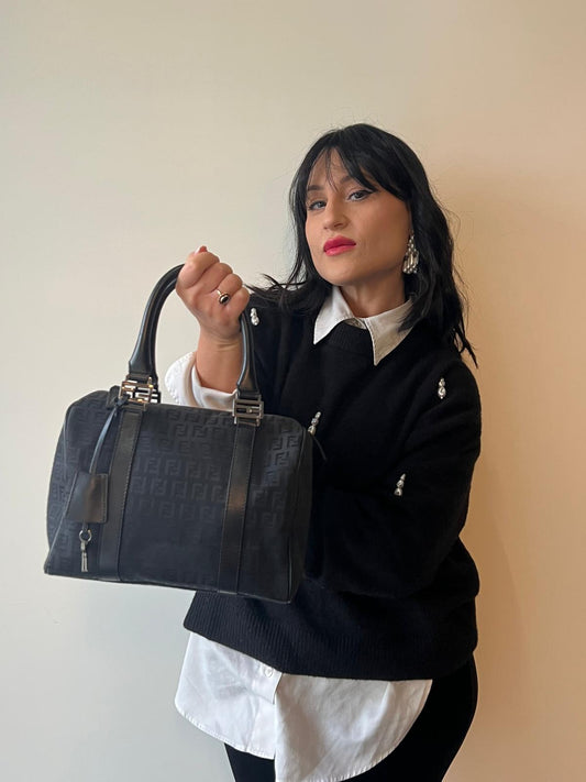 Ragazza che indossa una Borsa Fendi in tessuto nero trama Zucca con finiture in pelle tono su tono e parti metalliche argentate; munita di doppi manici stondati. Completa di chiavi e lucchetto. Originale, usato, di lusso, in ottime condizioni.