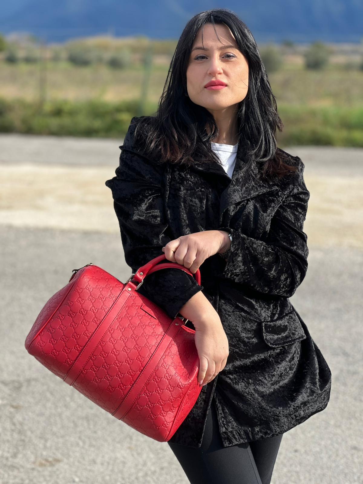 Ragazza che indossa una Borsa Gucci in pelle color rosso GG con parti metalliche dorate; munita di doppi manici stondati , da portare a mano. Completa di dustbag. Originale, usata, di lusso, in ottime condizioni.