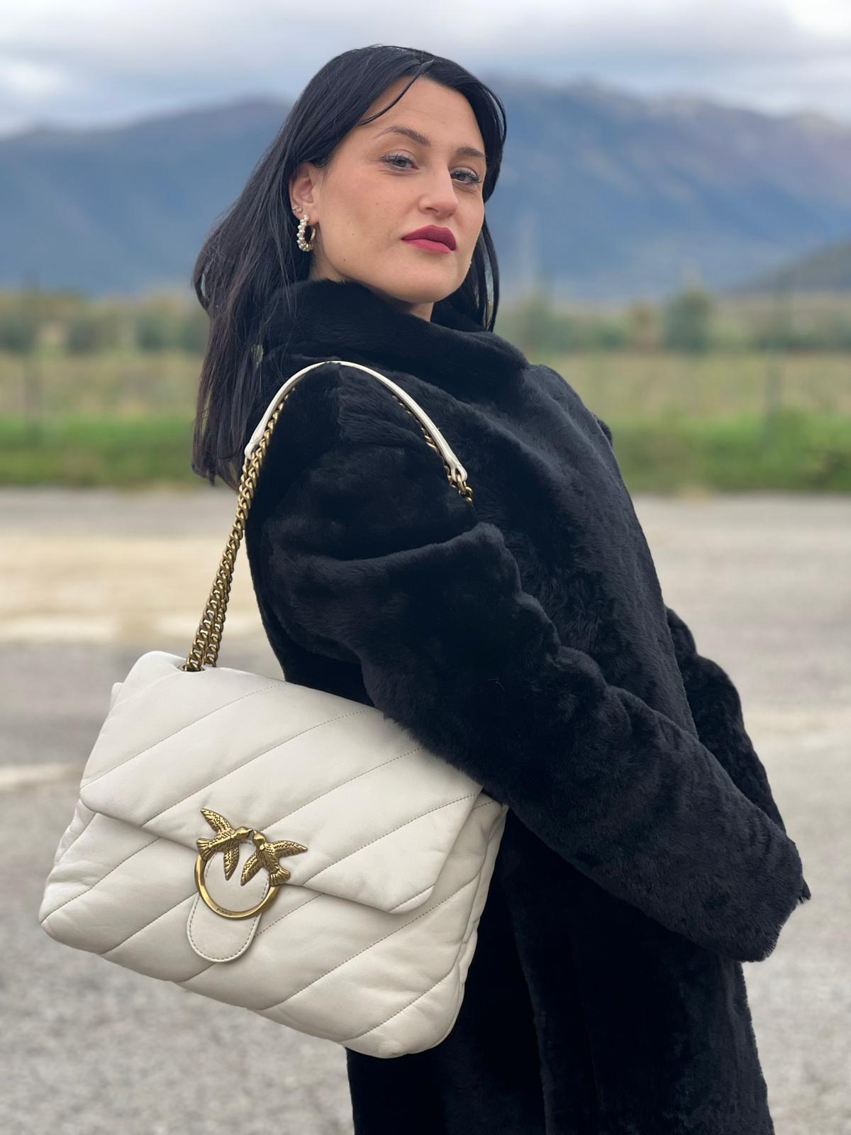 Ragazza che indossa una Borsa Pinko in pelle trapuntata color bianco gesso con parti metalliche dorate; munita di una tracolla in catena scorrevole e spallaccio in pelle. Indossabile a spalla oppure a tracolla. Originale, usata, di lusso, in condizioni buone.